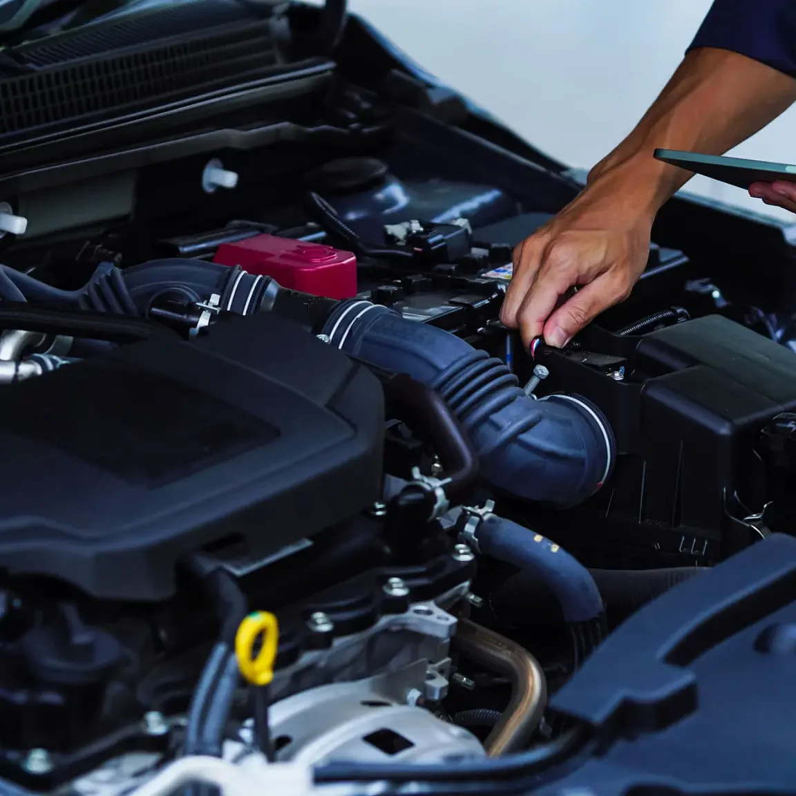 Mechanic inspecting car engine with tablet.